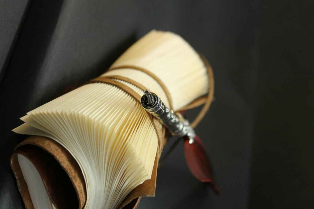 A diary is rolled and tied with string and a feather pen is placed on it.